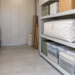 棚の上で袋入りの寝具とケースを保管し、通路を空けた収納庫